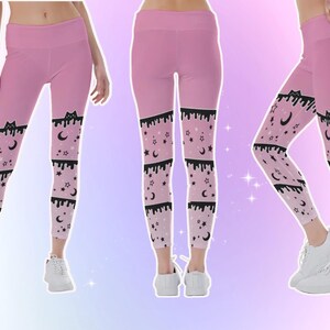 Może przedstawiać: R&oacute;żowe legginsy z wysokim stanem i czarno-białym wzorem. Wz&oacute;r zawiera sylwetkę kota, spływające linie, gwiazdy i p&oacute;łksiężyce. Legginsy są pokazane z wielu perspektyw.