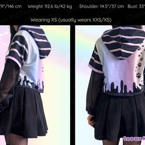 May include: A two-piece outfit featuring a black pleated skirt and a cropped hoodie. The hoodie has a white, blue, and pink color scheme with black stripes and dripping paint details. The outfit is designed with a unique aesthetic.