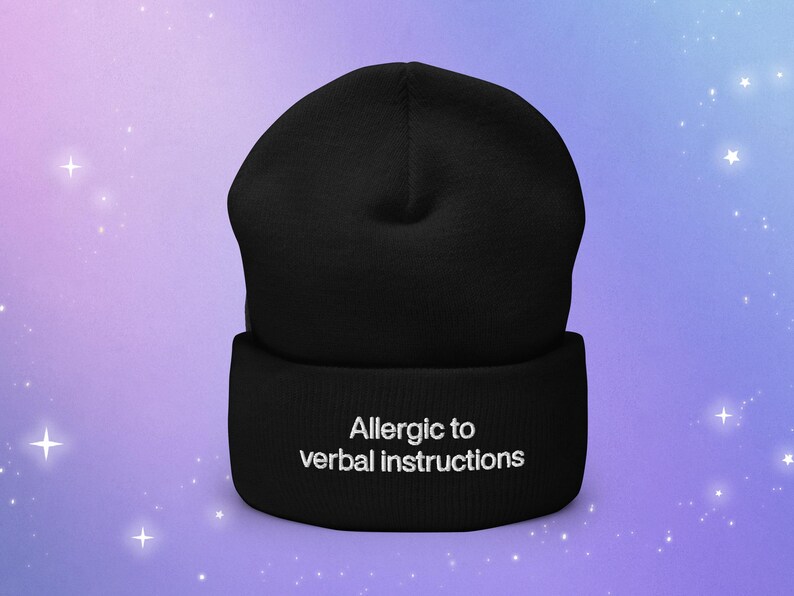 Op de afbeelding: Zwarte beanie met witte tekst die "Allergie voor verbale instructies" zegt.