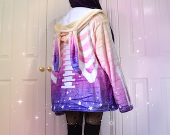 Könnte beinhalten: Ein Plüsch-Hoodie mit einem Regenbogen-Ombre-Design und einem weißen Skelett-Druck. Der Hoodie hat Hasenohren an der Kapuze.