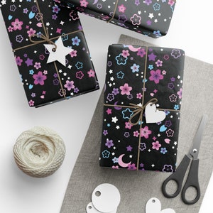 May include: Three gift boxes wrapped in black paper with a pink and blue floral pattern. The boxes are tied with twine and decorated with white paper stars and hearts.