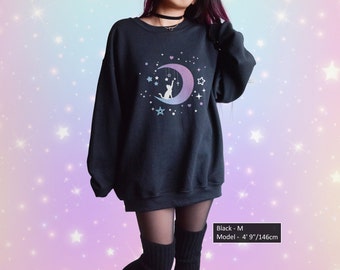 May include: Black sweatshirt with a graphic of a cat sitting on a crescent moon with stars. The moon is a gradient of pink and blue. The text "Black - M" and "Model - 4' 9"/146cm" is at the bottom of the image.