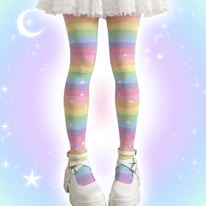 Peut inclure: Collants opaques à rayures horizontales arc-en-ciel pastel dans des tons de rose, jaune, vert, bleu et violet, ornés de petits motifs d'étoiles blanches. Les collants sont portés avec des chaussures à plateforme blanches et un ourlet de jupe à volants.