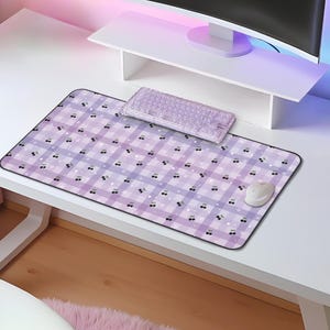 May include: A purple and white checkered mouse pad with a small black and white design. The mouse pad is on a white desk with a computer monitor and a keyboard.