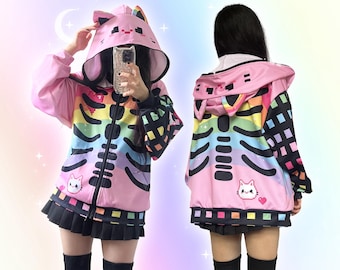May include: Pink zip-up hoodie with a rainbow skeleton design. The hoodie has a cat-ear hood, rainbow accents, and a black and white checkered pattern on the sleeves. A small cat graphic is on the front. The model is wearing a black pleated skirt.