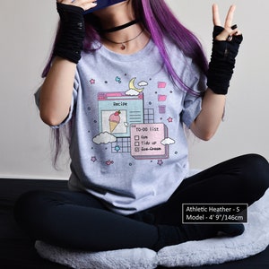 May include: A heather grey t-shirt featuring a graphic of a computer screen with a recipe and a to-do list. The graphic includes a pink ice cream cone, a blue cloud, and a yellow moon. The text on the shirt reads "Recipe" and "To-Do List". The model is wearing a size S.