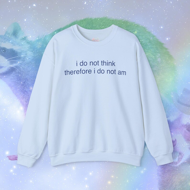 May include: A white sweatshirt with the text "i do not think therefore i do not am" in blue. The long-sleeved crew neck top is a casual style. The background features a raccoon and a rainbow-colored design.