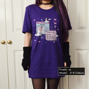 May include: Purple t-shirt featuring a graphic of a computer screen displaying a to-do list with the text "Recipe", "TO-DO list", "Gym", "Tidy up", and "Ice Cream". The model is 4' 9"/146cm tall and wearing a size XS.