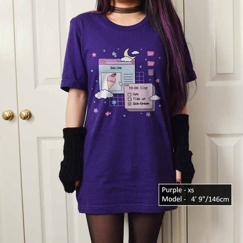 May include: Purple t-shirt featuring a graphic of a computer screen displaying a to-do list with the text "Recipe", "TO-DO list", "Gym", "Tidy up", and "Ice Cream". The model is 4' 9"/146cm tall and wearing a size XS.