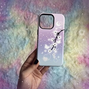 Op de afbeelding: Een witte telefoonhoes met een paarse en roze ombre achtergrond. De hoes heeft een zwart silhouet van een tak met witte bloemen en vlinders. De achtergrond is bedekt met kleine witte sterren.