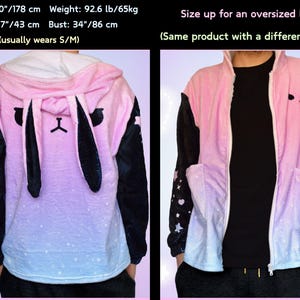 Puede incluir: Sudadera con capucha de color rosa y azul degradado con mangas negras y una cara de conejo negra en la parte delantera. La sudadera tiene una cremallera y una capucha con orejas de conejo. La sudadera est&aacute; decorada con estrellas blancas.