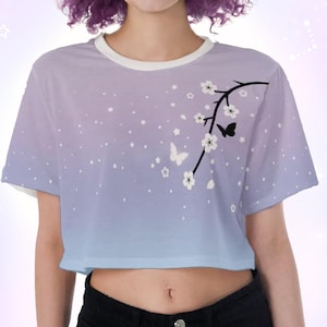 May include: A purple and blue ombre crop top with a white floral design and black butterflies. The top has a white ribbed crew neck.