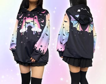 May include: Black hoodie with a colourful rainbow, bats, and stars design. The sleeves have a pastel gradient. The hood features bat ears. The back of the hoodie has a bat wing design. The hoodie is worn with a black skirt.