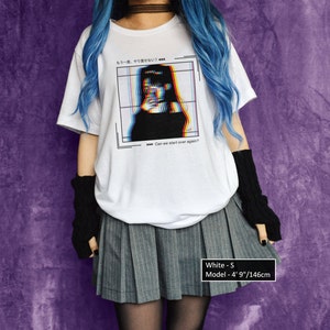 K&ouml;nnte beinhalten: Wei&szlig;es T-Shirt mit einem Grafikdruck eines Frauen Gesichts mit Glitch-Effekt. Der Text auf dem Shirt lautet "もう一度、やりせない" und "Can we start over again?" Das Model tr&auml;gt ein wei&szlig;es T-Shirt, einen grauen Faltenrock und schwarze fingerlose Handschuhe. Das Model ist 146 cm gro&szlig;.