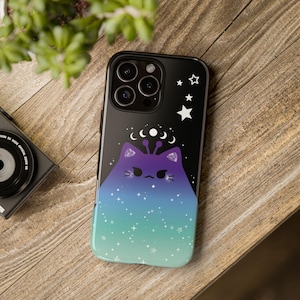 May include: A black phone case with a purple and blue galaxy design. A cartoon cat with a crown of stars and moons is in the center of the design.