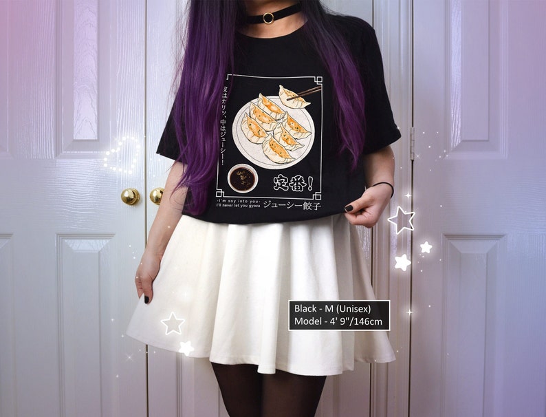May include: Black t-shirt with a graphic of a plate of dumplings and chopsticks. The text on the shirt says "I'm so into you... I'll never let you go... Juicy Gyoza!" and "定番!" in Japanese. The model is wearing a white skirt and is 4' 9" tall.
