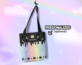 May include: Black tote bag with a rainbow and stars design. The bag has a white cat with a pink nose and the name "Amanda" written below it. The bag has black cat paw prints and crescent moons on the bottom.