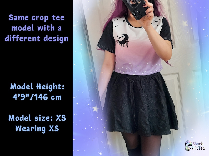 May include: A cropped t-shirt with a white background and a pink to purple ombre design. The shirt has a black crescent moon with a dripping black design and white stars. The model is wearing a black skirt and is 4'9"/146 cm tall.  Model size: XS. Wearing XS.