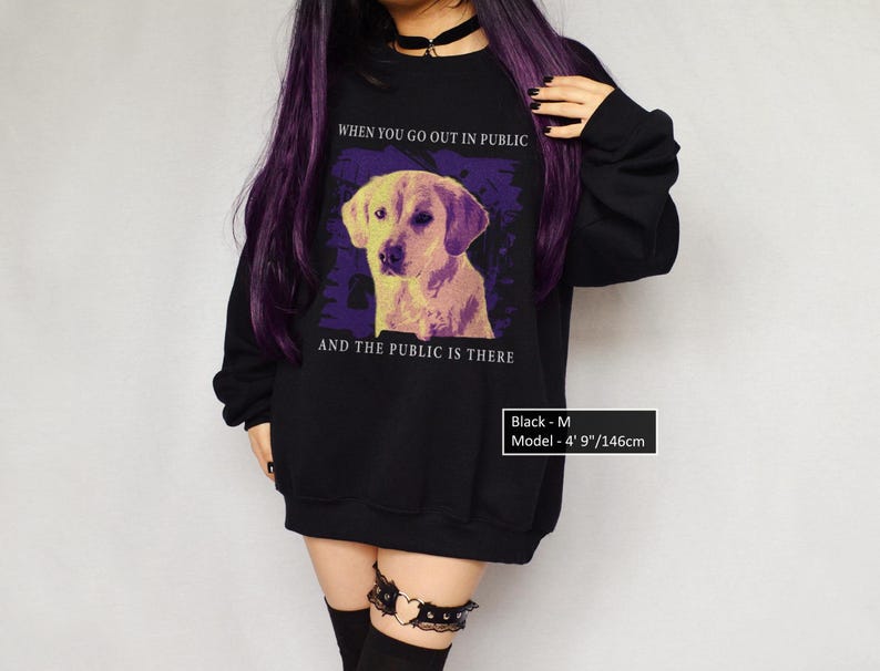 a girl wearing a black an oversized sweatshirt with the text WHEN YOU GO OUT IN PUBLIC AND THE PUBLIC IS THERE
the graphic is a golden retriever dog in public,  in style of vintage, in yellow and purple tones