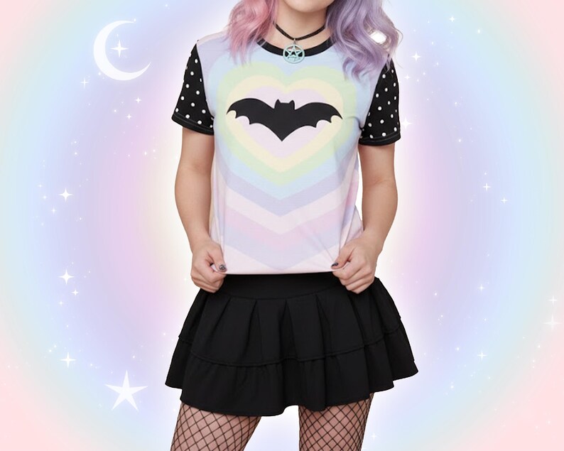 May include: A black bat graphic is centered on a pastel rainbow heart design on a short-sleeved t-shirt. The shirt has black sleeves with white polka dots. A black pleated skirt and fishnet stockings complete the outfit.