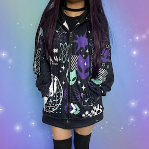 May include: Black zip-up hoodie with a colorful graphic print featuring geometric shapes, stars, and alien-like creatures. The print includes the text "SPACE 1994".