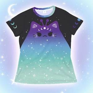 Op de afbeelding: Zwart T-shirt met een kattenontwerp in paarse, blauwe en groene tinten. De kat heeft maanvormige accenten en antennes. Het shirt heeft een gradiënteffect, van zwart naar groen met sterren.