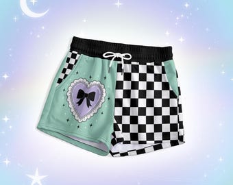May include: Athletic shorts featuring a split design with a solid mint green side and a black and white checkered side. The mint green side displays a lavender heart graphic with a white lace border and a black bow. Includes a black waistband and white drawstring.