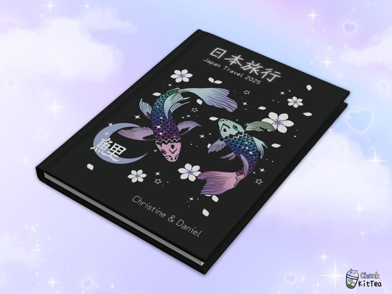 May include: A black journal with a Japanese design featuring two koi fish, cherry blossoms, and the text "日本旅行 Japan Travel 2025". The journal also has the text "Christine & Daniel" on the front cover.