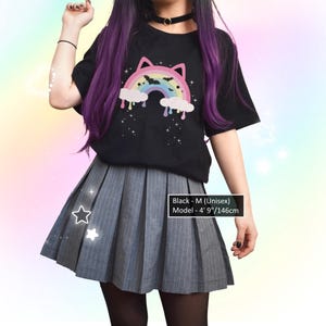 K&ouml;nnte beinhalten: Schwarzes Unisex-T-Shirt mit einem Regenbogen-Katzen-Design, kombiniert mit einem grauen Faltenrock. Das Model ist 146 cm gro&szlig;. Das Shirt zeigt einen bunten Regenbogen, Wolken und Sterne.