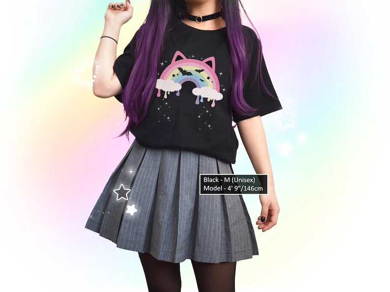 K&ouml;nnte beinhalten: Schwarzes Unisex-T-Shirt mit einem Regenbogen-Katzen-Design, kombiniert mit einem grauen Faltenrock. Das Model ist 146 cm gro&szlig;. Das Shirt zeigt einen bunten Regenbogen, Wolken und Sterne.