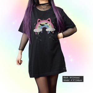 K&ouml;nnte beinhalten: Schwarzes Unisex-T-Shirt mit einem Regenbogen-Design mit Katzenohren, Flederm&auml;usen und tropfenden Wolken. Das Shirt ist in Gr&ouml;&szlig;e M und das Model ist 146 cm gro&szlig;. Teil einer Gothic- oder alternativen Modekollektion.