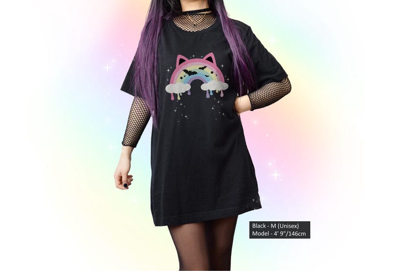 K&ouml;nnte beinhalten: Schwarzes Unisex-T-Shirt mit einem Regenbogen-Design mit Katzenohren, Flederm&auml;usen und tropfenden Wolken. Das Shirt ist in Gr&ouml;&szlig;e M und das Model ist 146 cm gro&szlig;. Teil einer Gothic- oder alternativen Modekollektion.