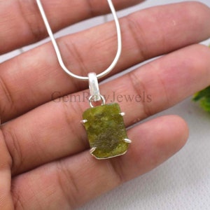 Op de afbeelding: Een zilveren hangerketting met een rechthoekige, olijfgroene edelsteen. De steen is gezet in een zilveren zetting en hangt aan een fijne zilveren ketting. De hanger heeft een natuurlijk, getextureerd uiterlijk.