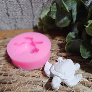 Könnte beinhalten: Eine rosa Silikonform zum Herstellen einer kleinen Schildkrötenfigur. Neben der Form ist eine weiße Schildkrötenfigur zu sehen.