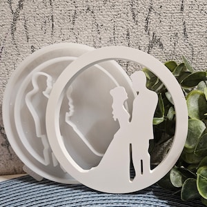 Könnte beinhalten: Weiße Harzformen mit Hochzeitsmotiv. Eine Form zeigt eine Silhouette von Braut und Bräutigam in einem Kreis, während die andere ein Seitenprofil eines Paares zeigt. Die Formen dienen zur Herstellung von Dekorationsartikeln für Hochzeiten und Feiern.