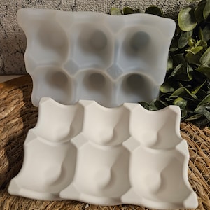 Könnte beinhalten: Zwei weiße Eierkartons, übereinander gestapelt. Der obere Karton besteht aus einem flexiblen, durchsichtigen Material. Der untere Karton besteht aus einem festen, undurchsichtigen Material.