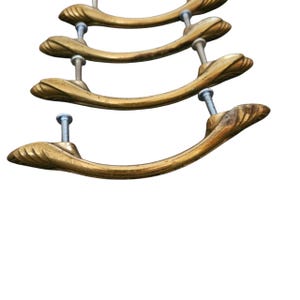 May include: Four antique brass drawer pulls with a curved design and decorative end details. Each pull is attached with a silver screw. The pulls are arranged vertically against a white background, showcasing their vintage aesthetic.
