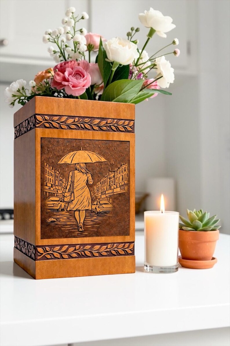 Elegant handcrafted wooden urn box for ashes with a unique umbrella rain walk engraving design. The detailed artwork shows a peaceful figure walking along a city street, symbolizing remembrance and life's journey. This wooden cremation urn includes carved border accents and a warm natural wood finish, making it a meaningful memorial keepsake.
