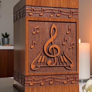 Puede incluir: Una caja de madera con temática musical. La caja es de color marrón cálido y presenta notas musicales talladas, una clave de sol y teclas de piano. El diseño se repite alrededor de los bordes superior e inferior.