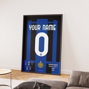 Puede incluir: Un póster enmarcado en negro con un fondo a rayas azul y negro. El póster presenta un número blanco "0" y el texto "YOUR NAME" en la parte superior. El póster también incluye el logotipo del Inter de Milán y el texto "Giuseppe Meazza 45°46' N 9°09' E Milán 1908".