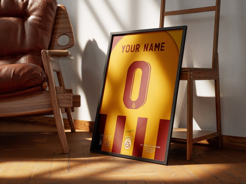 May include: A framed print of a yellow and red soccer jersey with the number 0 on the front. The jersey has a black frame and the text "YOUR NAME" at the top. The jersey also has a small logo on the bottom left corner.