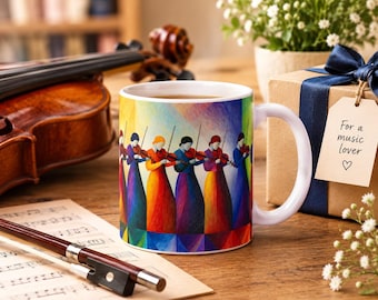 May include: A white ceramic mug featuring a colorful illustration of multiple violinists in vibrant, long dresses playing violins. The mug is positioned near a wooden violin, a bow on sheet music, and a gift box with a tag reading For a music lover.