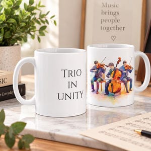 May include: Two white ceramic mugs. One mug features the black text "TRIO IN UNITY" in a serif font. The second mug displays a colorful watercolor illustration of three musicians playing a violin, a cello, and a viola while seated on chairs.