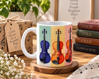 May include: A white ceramic mug featuring a colorful illustration of three string instruments, including a blue violin, an orange violin, and a reddish-brown violin, each set against a vertical panel of textured light blue, yellow, and pink.