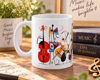 May include: A white ceramic mug featuring a colorful abstract illustration of musical instruments including a red cello, geometric shapes, and black line art. The mug has a smooth finish and a curved handle, displaying a vibrant artistic design.
