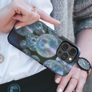 May include: A black phone case with a design of silver disco balls. The phone case has a camera lens with three black circles.