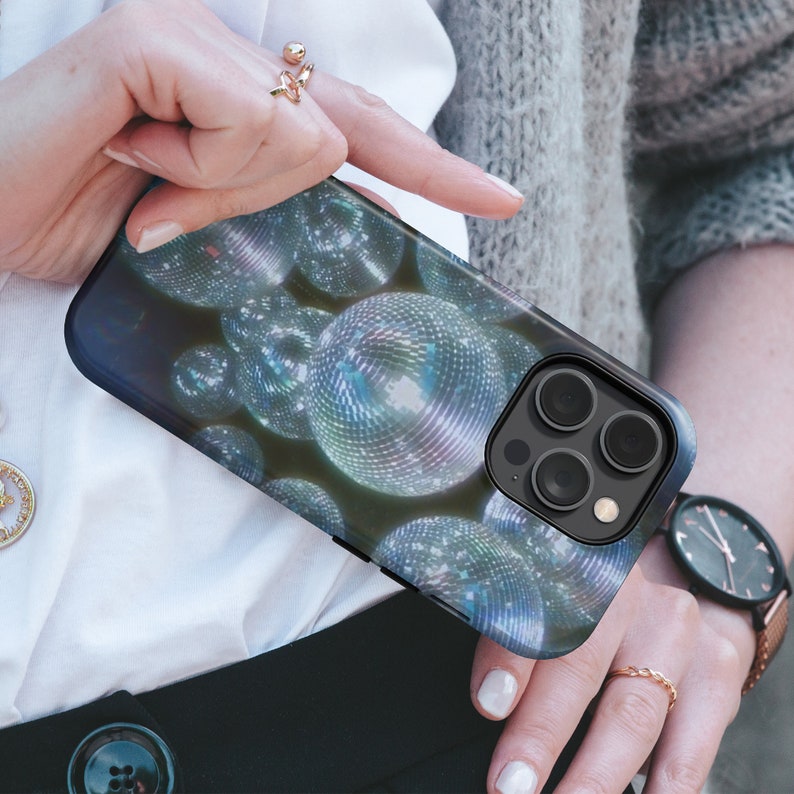 May include: A black phone case with a design of silver disco balls. The phone case has a camera lens with three black circles.