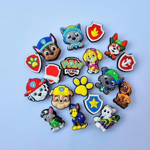 May include: A set of 15 colourful Paw Patrol shoe charms featuring characters such as Chase, Marshall, Skye, and Rubble. The charms are made of rubber and have a variety of designs, including paw prints, shields, and the Paw Patrol logo.