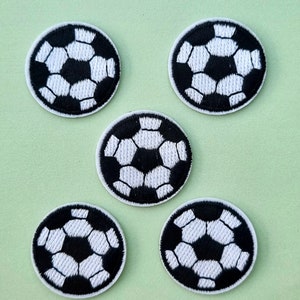 May include: Five circular patches with a football design. Each patch features a black and white pattern, with the football's pentagons and hexagons clearly defined. The patches are set against a light green background.