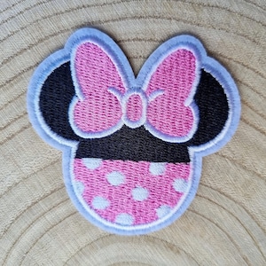 May include: Pink and black embroidered iron-on patch featuring a cartoon character with a bow and polka dots.